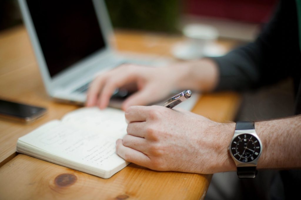 Person taking notes next to a laptop