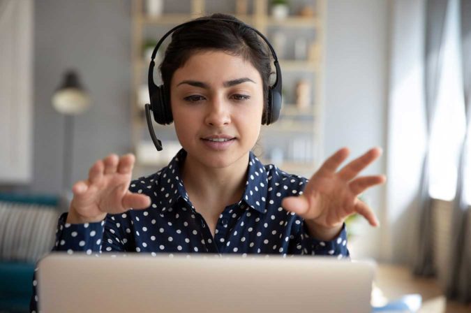 A women wearing a headset and gesturing at a computer monitor